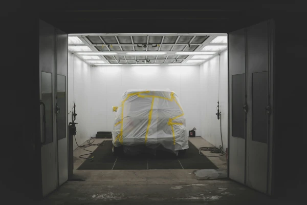 a car covered in a white cover in a garage by a car spray painter